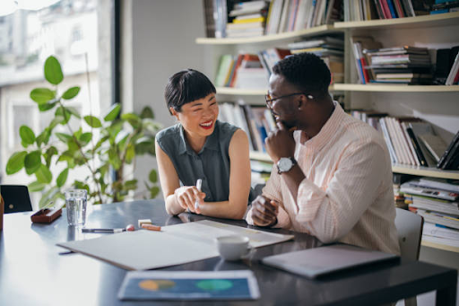 Two colleagues discuss IFZA Free Zone license fees in a modern, book-filled office setting.